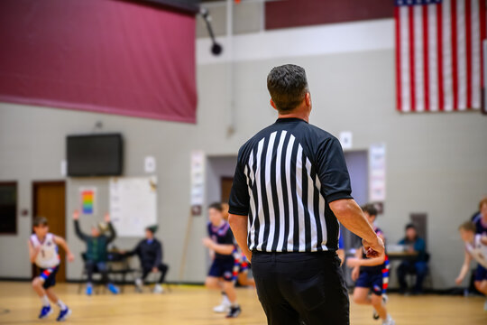 Basketball game in school gym with referee overseeing young players during match in early evening hours