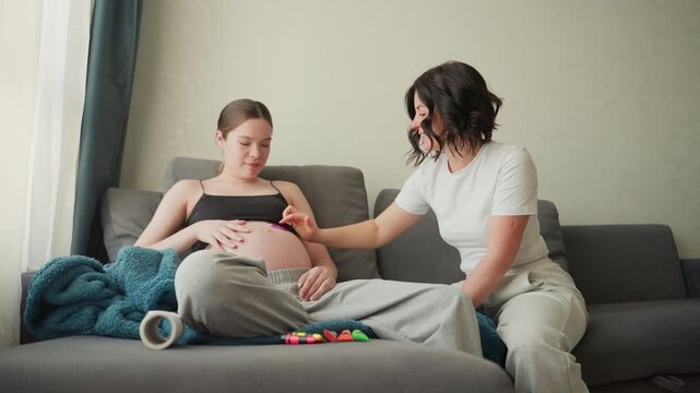 Pregnant woman on sofa receiving doula care intimate prenatal moment at home seated expecting mother in casual clothes smiles while support person gently touches belly soft natural light cozy blanket