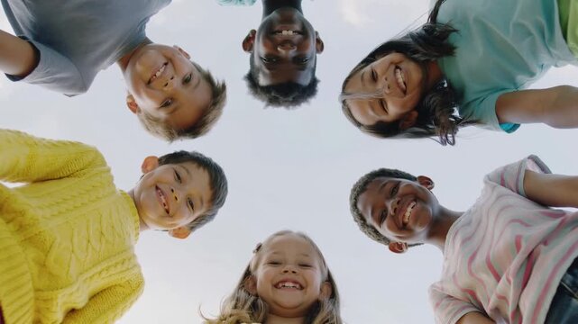 Diverse group of children looking down at camera in low angle view against clear sky
