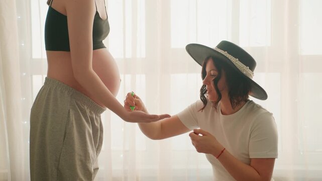 Pregnant woman art. Serene pregnant woman carefully embellishes belly alongside close companion. Tranquil expectant mother elegantly decorating her belly with supportive friend nearby