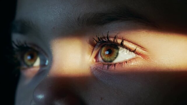 Young woman hazel eyes illuminated by golden light in extreme close up shot