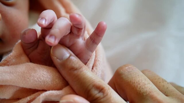 Newborn baby hand holding adult finger wrapped in soft peach blanket close up