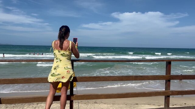 Young latin american woman in yellow dress taking photo of the beach sea view