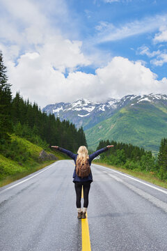 Backpack, woman and arms up on road with mountain view, sightseeing and travel exploration for vacation. Back, person and adventure outdoor with scenery for winter holiday, hiking trip and freedom.
