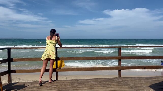 Woman taking photo with smartphone on pier overlooking tropical beach