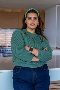 Adult female standing at kitchen island wearing green sweater, smartwatch, with stovetop backdrop