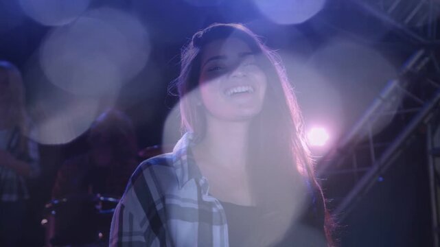 Lead female performer shifting smile into song on music stage, backlight causing bokeh across face
