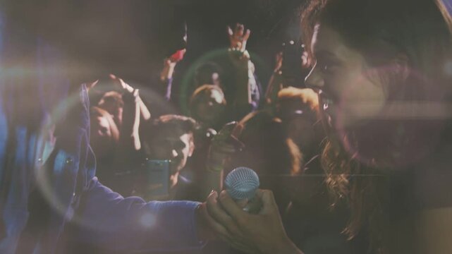 Performer offering mic to fan to sing at concert; phones filming, animated flares highlighting mic