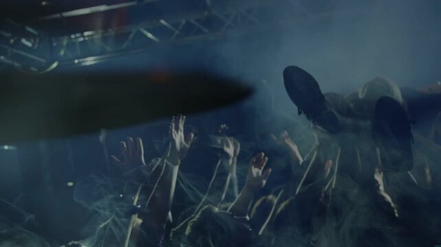 music crowd carrying crowd-surfer over raised hands, cheering, drumstick sweeping across cymbal