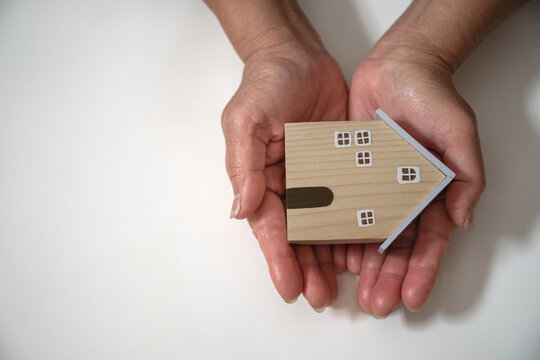 Hands hold small wooden house, symbolizing home protection, real estate security, family stability, insurance, and long-term investment, reflecting trust, safety, and responsible ownership.