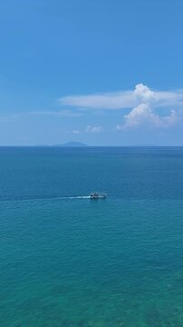 Sailboat Glides Peacefully on Vast Blue Sea with Distant Island and Hills Under Clear Sky, Evoking Tranquility on Ocean Horizon	