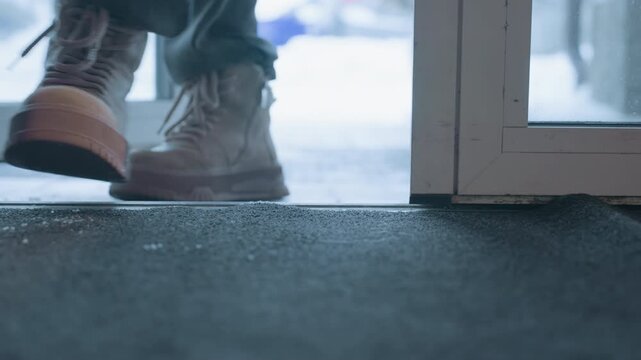 Hesitant boots pausing at cafe door, closeup of sole near mat and glass, cold air outside and warm interior promise, brief stillness before step suggests contemplation and careful entry