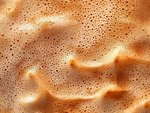 close-up of golden brown creamy coffee foam with dense microbubbles and smooth frothy waves, warm inviting cozy feeling