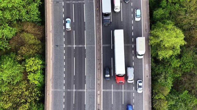 Top-down drone view of vehicles moving along a motorway in the UK. Cars and trucks driving in lanes, showcasing traffic flow, logistics, transportation and urban infrastructure.