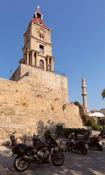 Clock tower above stone walls with scooters in old town of Rhodes Greece