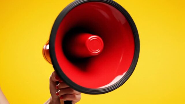 Hand Holding Red Megaphone Against Yellow Background Announcing Message.