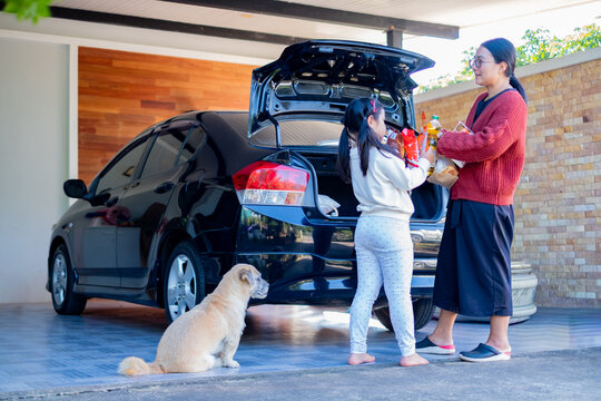 Asian mother and daughter opening car trunk to load groceries in a parking lot. Young girl helping her mom with a shopping cart after buying products at a supermarket. Family lifestyle concept.