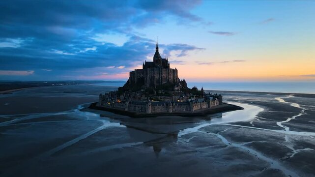 Epic aerial view of the illuminated Mont Saint Michel fortress at sunset with reflections on the water