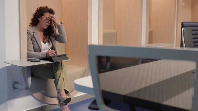 Stressed businesswoman working on tablet in modern office pod