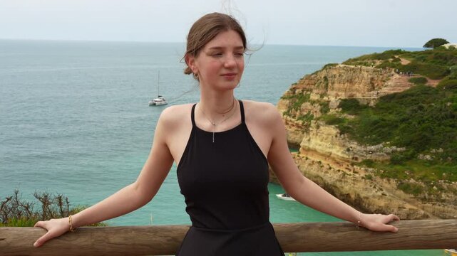 Happy young woman enjoying the fresh air and stunning ocean view from a cliffside viewpoint. Peaceful mood, ideal for travel and leisure content. Benagil, Algarve, Portugal