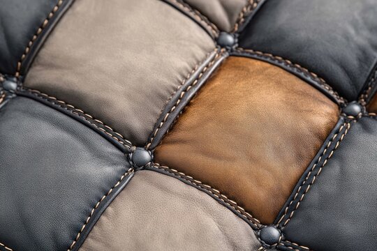 Close-up of tufted patchwork leather cushion with stitched seams and buttons, brown gray and black squares, warm inviting luxurious texture