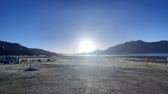 Stunning morning sun rising over a high-altitude lake in Tibet with horses and yaks in a lakeside enclosure.