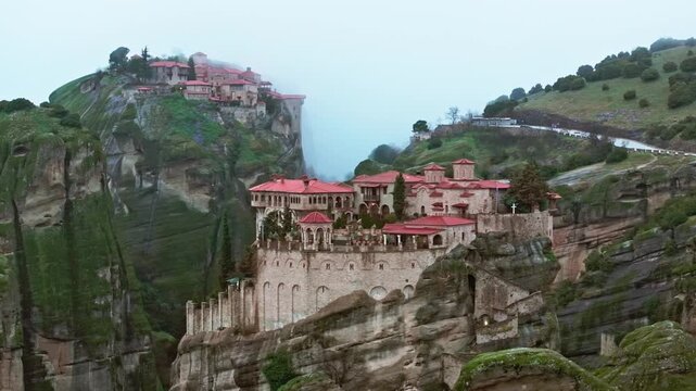 Breathtaking aerial drone footage of Meteora in Kalambaka, Greece, captured in a mystical foggy atmosphere. The iconic monasteries perched atop towering rock formations emerge through the mist, while 