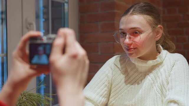White woman reviewing photos on camera in cafe, smiling glance at display with brick wall backdrop, conversational mood and gentle daylight through window, relaxed meetup and lifestyle documentation