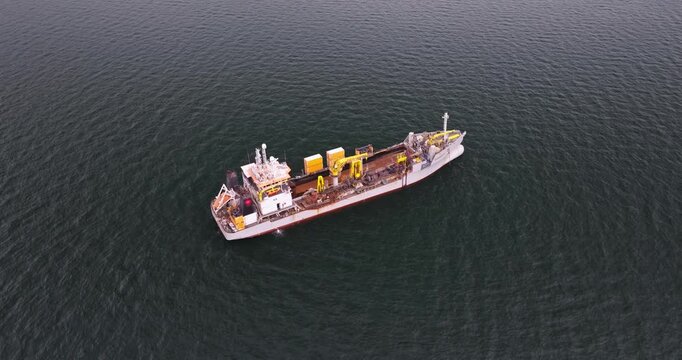 High-quality aerial footage of a dredger support vessel, also known as a subsea cable ship, operating in a busy industrial port. The vessel is designed for underwater cable installation, maintenance, 