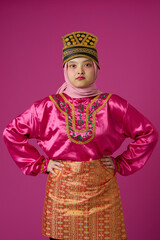 Naklejka premium Confident Indonesian Asian Woman in Bright Pink Traditional Costume and Hijab Wearing Ornate Gold Headdress