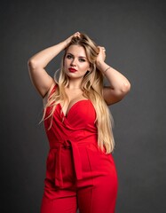 Fototapeta premium Attractive woman in red jumpsuit poses, hand over her head