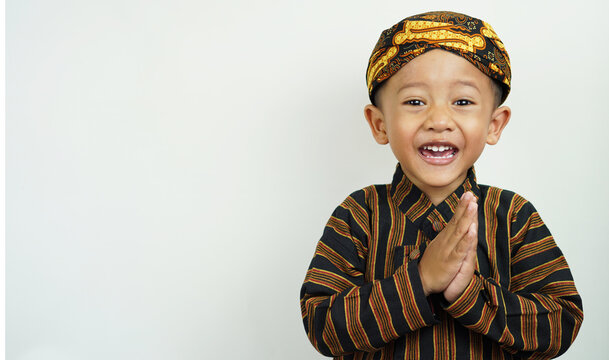 Portrait of a cute and handsome Asian boy of preschool age, wearing traditional East Javanese clothing, namely Baju Lurik complete with his blangkon while greeting and smiling sweetly,