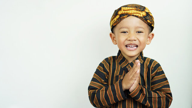 Portrait of a cute and handsome Asian boy of preschool age, wearing traditional East Javanese clothing, namely Baju Lurik complete with his blangkon while greeting and smiling sweetly,