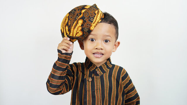 Portrait of a cute and handsome Asian boy of preschool age, wearing traditional East Javanese clothing, namely Baju Lurik complete with his blangkon while greeting and smiling sweetly.