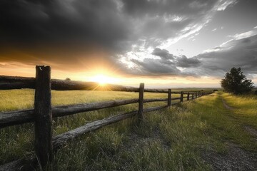 Fototapeta premium Sunset over rural grassy field with wooden split-rail fence and lone tree, peaceful golden light and dramatic clouds