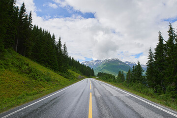 Fototapeta premium Landscape, forest and mountain with road in nature for travel, adventure and path for holiday. Clouds, woods and outdoor journey with scenic route, tourist highway and green foliage for vacation trip