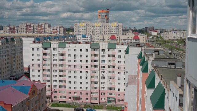 Urban apartment blocks from balcony overlooking pastel facades, rows of windows and green roofs under heavy clouds panoramic midrise residential neighborhood with rooftop structures, railings