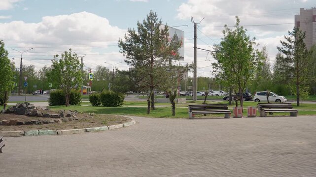 Bright urban park. Sunny green area with benches. Colorful city space filled with trees and benches. Illuminated metropolitan park surrounded by towering skyscrapers and seating zones
