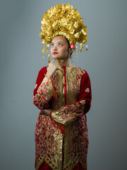 Naklejka premium Portrait of Indonesian Asian Woman in Traditional Red and Gold Costume Wearing Ornate Golden Headdress