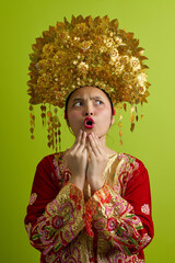 Naklejka premium Surprised Young Indonesian Asian Woman Wearing Ornate Golden Headdress and Traditional Embroidered Costume Portrait