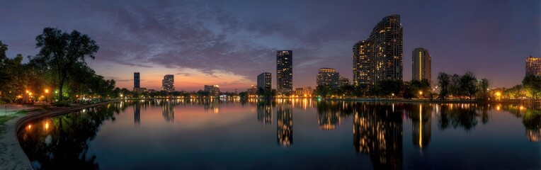 Fototapeta premium Panoramic view of a modern city skyline reflected in a calm lake at dusk.
