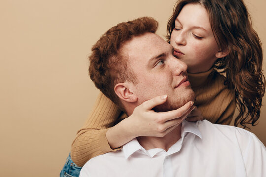 Young couple in casual clothes embraces tenderly on beige background. Woman holds man&rsquo;s face gently, expressing love and intimacy. Concept of romance, affection, and close relationship.