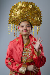 Naklejka premium Young Indonesian Asian Girl in Ornate Gold Headdress and Red Traditional Costume Smiling in Portrait