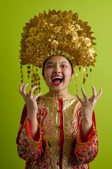 Naklejka premium Young Indonesian Asian Girl Wearing Ornate Gold Headdress and Traditional Embroidered Costume Screaming with Excitement