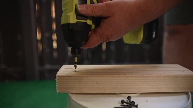 Man removing screw from wooden board using electric screwdriver tool creating process of disassembly and material removal during construction and carpentry work