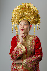 Naklejka premium Young Indonesian Asian Girl in Gold Floral Headdress and Embroidered Red Traditional Costume Looking Surprised
