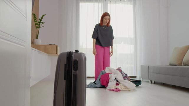 A woman tries to fit more clothes into a suitcase that is already full. She faces challenges as she tries to close it. The scene takes place in a bright living room.