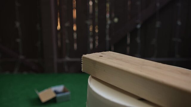 Man driving screw into wooden board with electric screwdriver close up creating process of assembly and fastening materials during construction and carpentry work