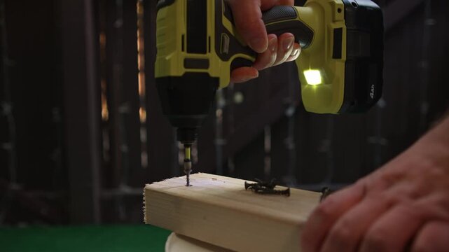 Man extracting screw from wood using electric screwdriver during work creating process of fastener removal and element disassembly during construction tasks