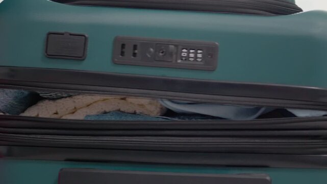 Hands are seen zipping up a suitcase. This action shows someone getting ready for a vacation. Clothes and personal items are organized inside the luggage for travel.